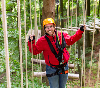 man holding onto a rope obstacles standing on logs in an adult challenge course